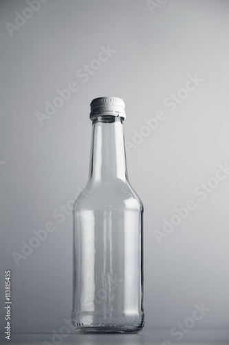 Empty unlabeled glass transparent bottle isolated on gray background in center