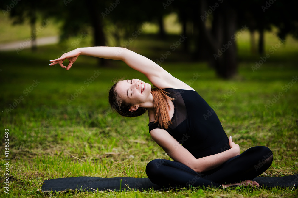 Fototapeta premium Happy, smiling, young woman resting on the grass at the park after the yoga. She is wearing dark leggings.