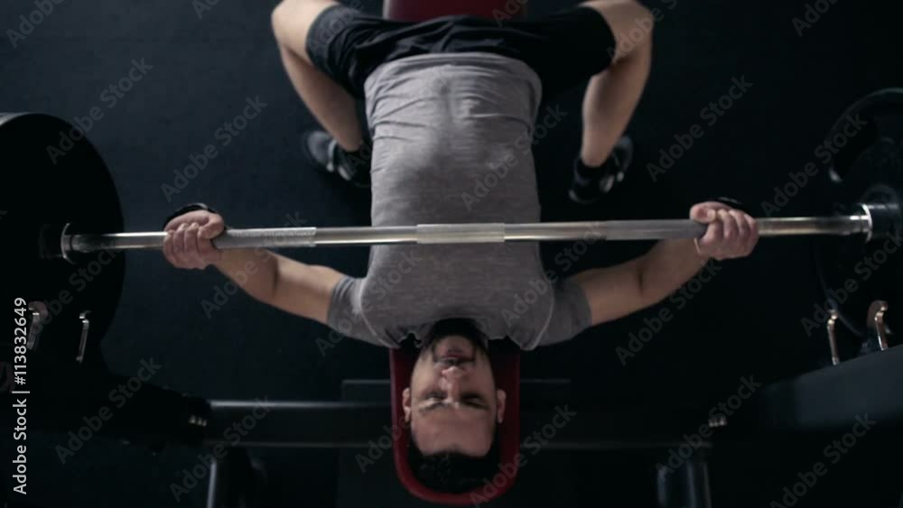 Young Male Athlete Raises The Barbell Lying In The Gym