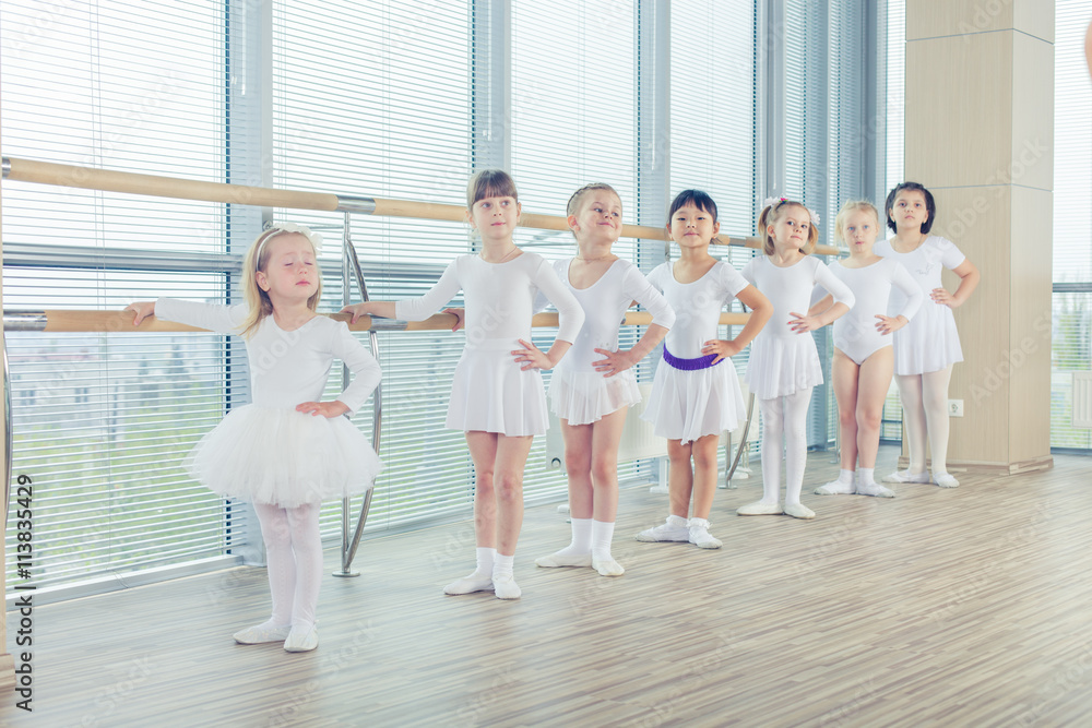 Group of seven little ballerinas standing in row and practicing ballet using stick on the wall Group of seven little ballerinas standing in row and practicing ballet using stick on the wall