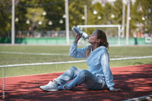 Young beautiful sportswoman resting after training. Woman drinking water