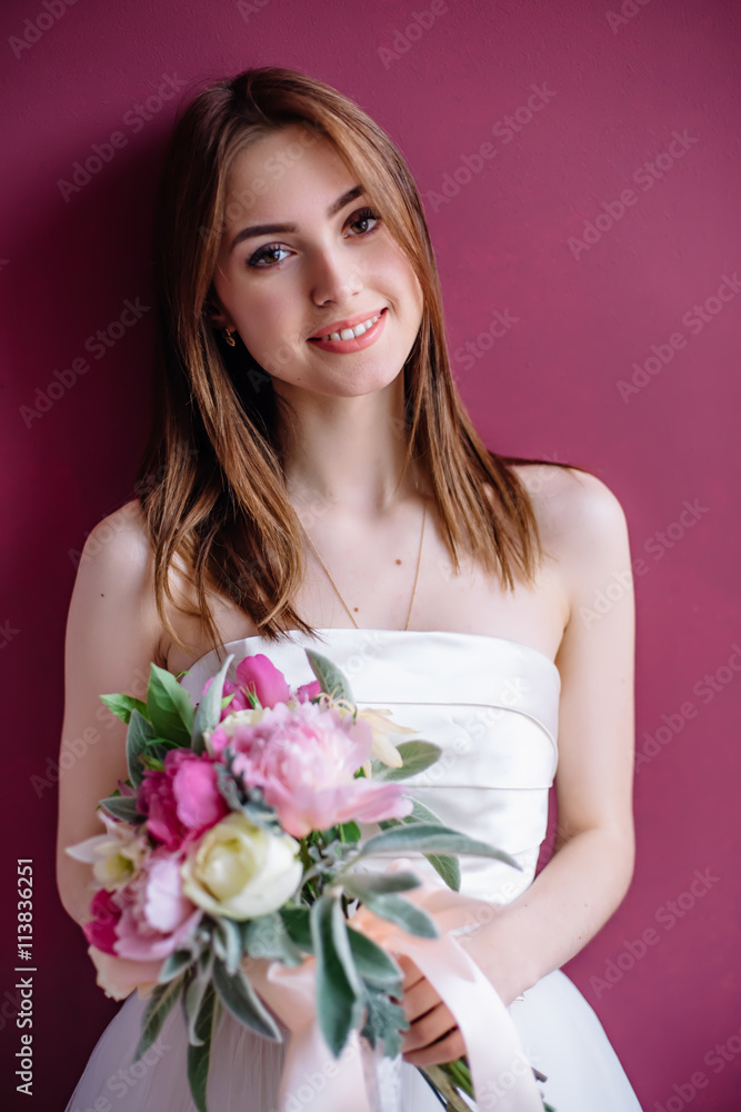 young beautiful bride with a bouquet of pink peony near the wall