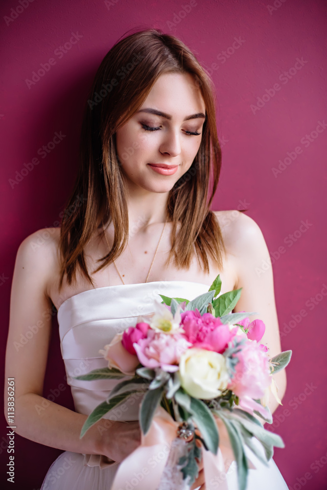 young beautiful bride with a bouquet of pink peony near the wall