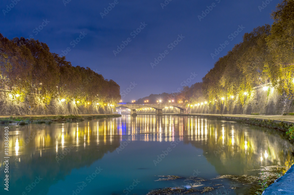 Fototapeta premium Old stone bridge on the river Tiber in Rome, lit at night