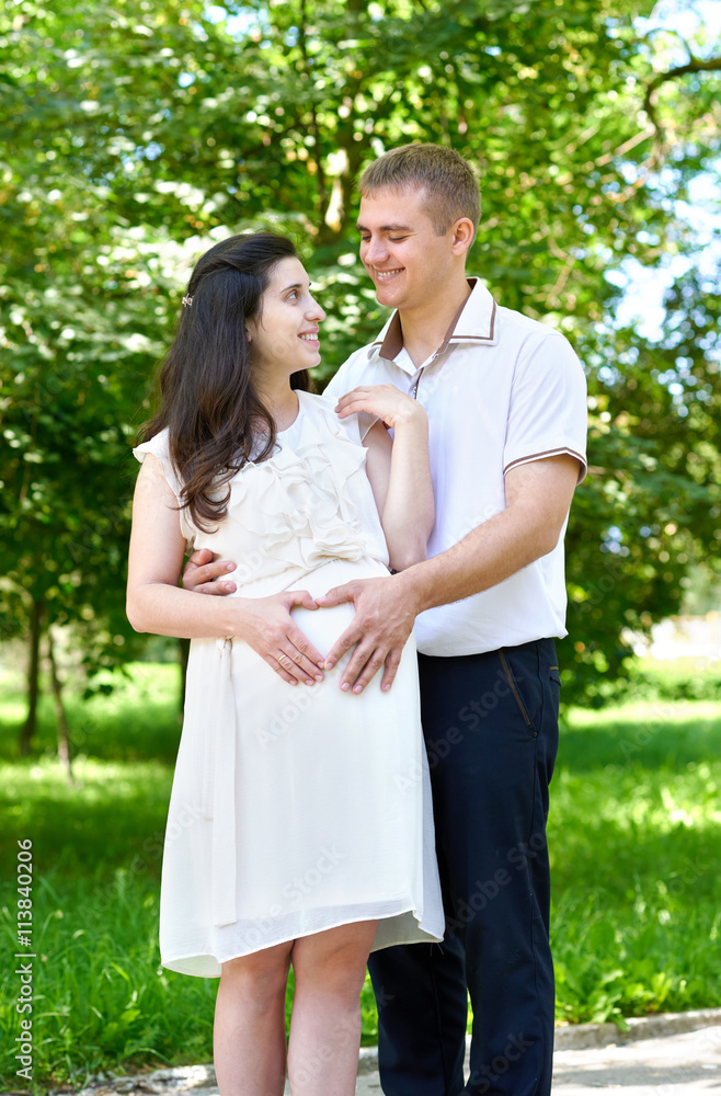 pregnant woman with husband posing in the city park, family portrait, summer season, green grass and trees