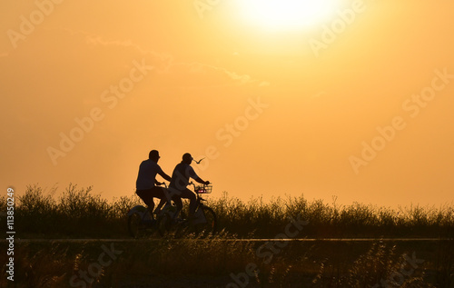 Couple riding bicycle on sunset sky, silhouette.
