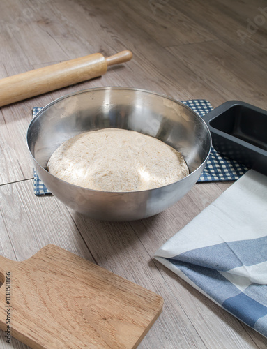 bread dough in stainless steel bowl and baking utensils on wooden background