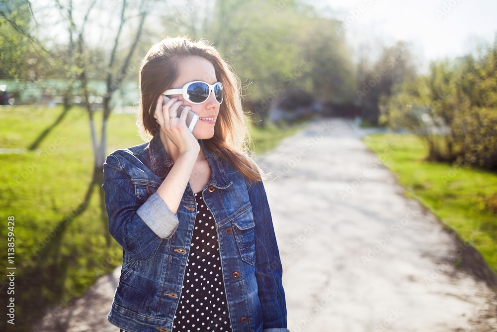 Young girl with sunglasses talking on a cell phone on a bright summer day. Young woman gossip