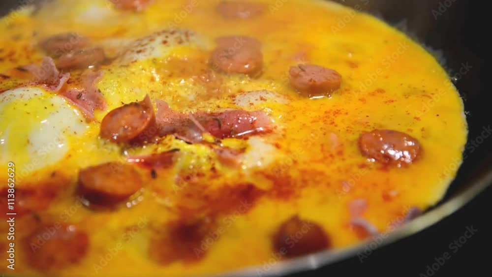 Frying ham and eggs with cheese, sausages and pepper in pan sprinkled by caraway seeds closeup. Frying ham and eggs with cheese, sausages and pepper in pan sprinkled by caraway seeds closeup.