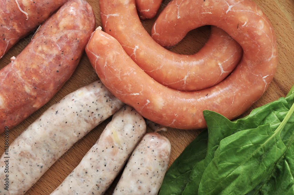 raw sausages for a barbecue with spinach leaves on wooden plate