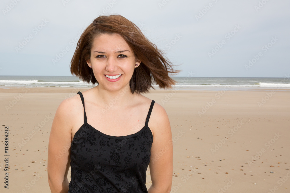 Smiling brunette girl in black dress posing on the beach Smiling brunette girl in black dress posing on the beach