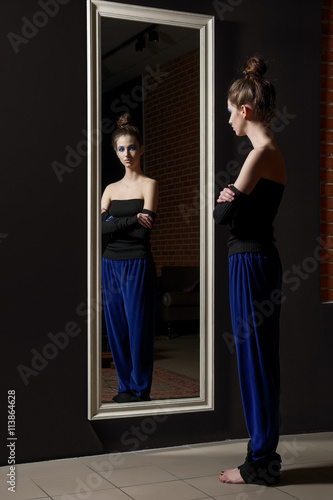 Pretty young model in fashion trousers and wool top near wall mirror
