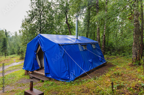 Military tent with stove and chimney pipe in a summer forest