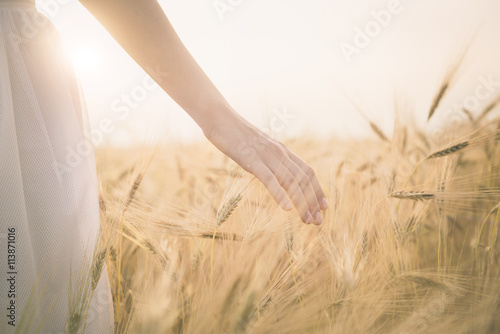 Foto Young girl walking through the field and touches wheat.