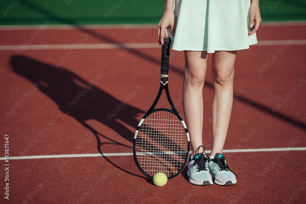 Legs of sportive girl near the tennis racquet and balls on tenni