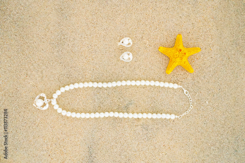 Starfish and pearl necklace on the white sand at the beautiful beach on sunny day.
