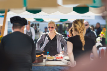 Beautiful blonde caucasian lady buying freshly prepared meal at a local street food festival. Urban international kitchen event in Ljubljana, Slovenia, in summertime.