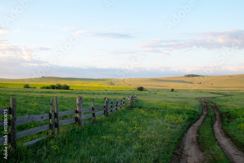 Rural road and an old fence in the early morning. The summer sunrise in the steppe of southern Siberia