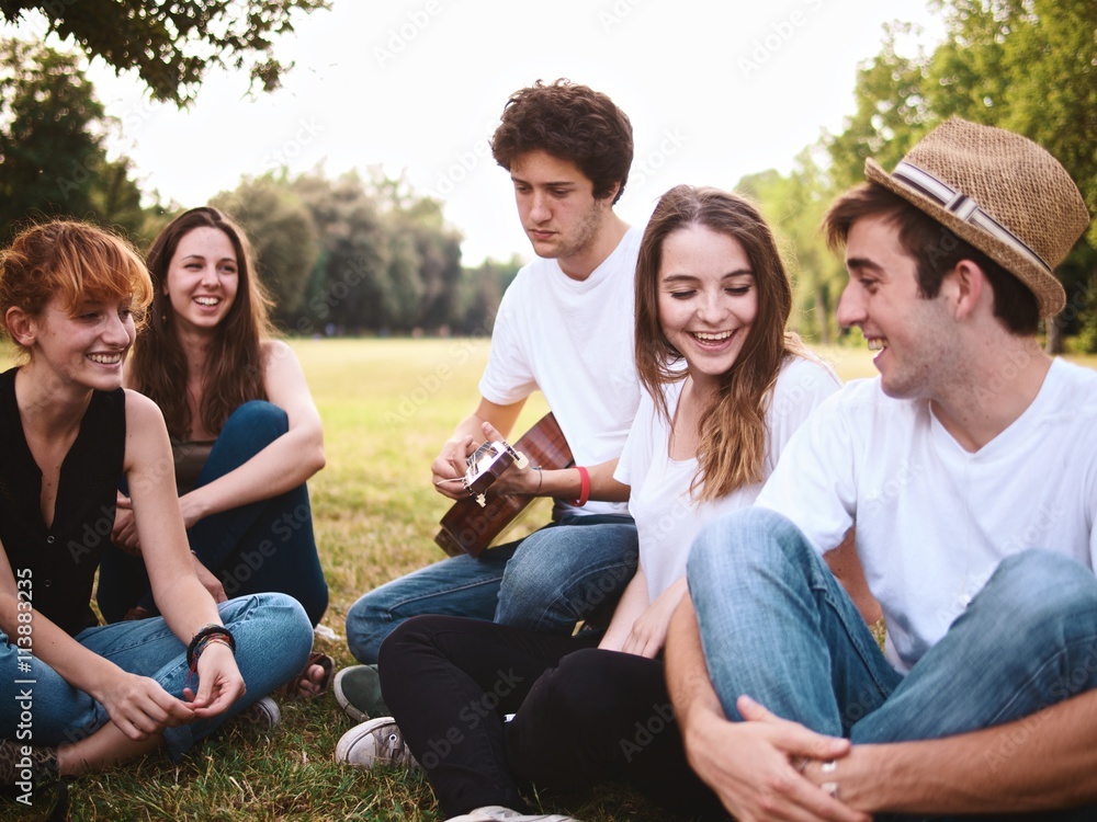 group of friends together in a park having fun and playing music with a guitar