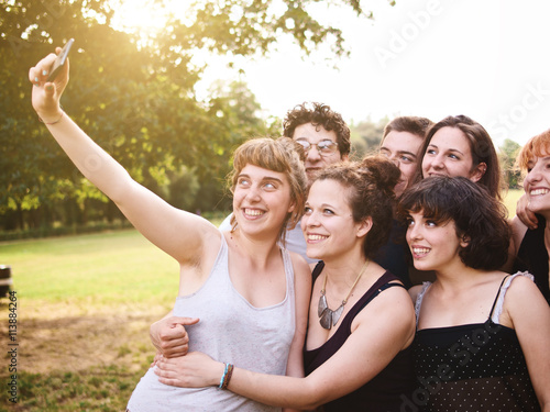 large group of friends together in a park having fun and taking a selfie with smartphone