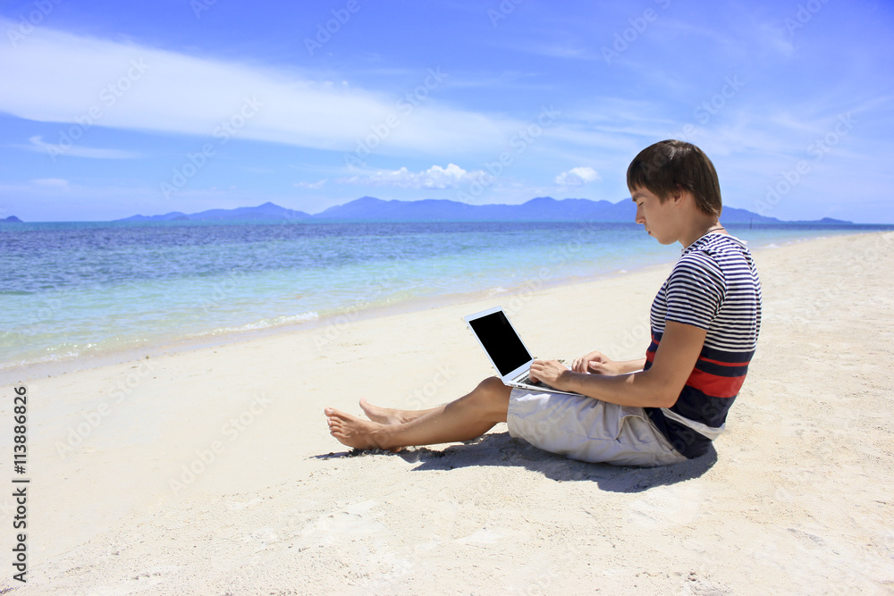 Business man working at a laptop on the beach with azure sea and white sand