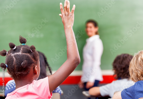 Happy schoolchildren at primary school raising hand in elementar