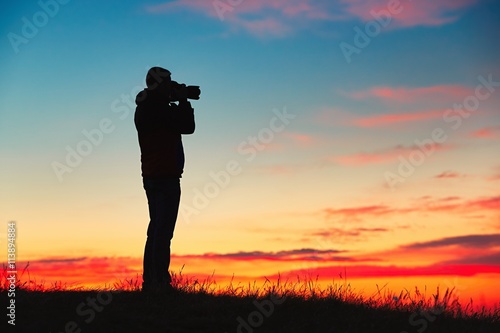 Silhouette of young photographer is enjoying sun. Photographer at the sunrise