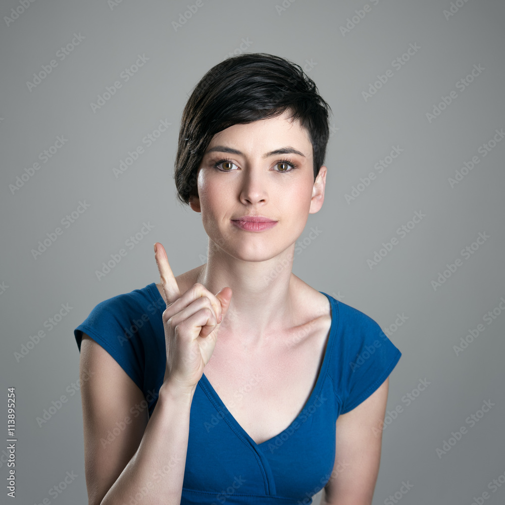 Smiling young short hair woman scolding finger looking at camera over gray studio background Smiling young short hair woman scolding finger looking at camera over gray studio background