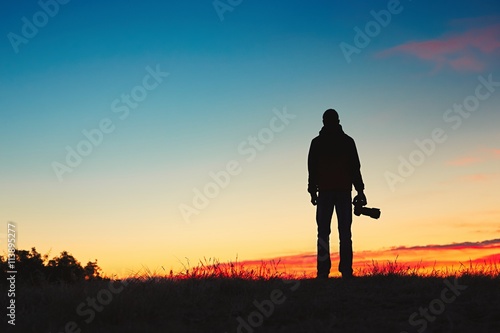 Silhouette of young photographer is enjoying sun. Photographer at the sunrise