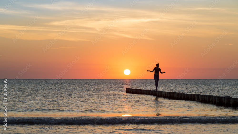 woman is balancing on a groin at sunset