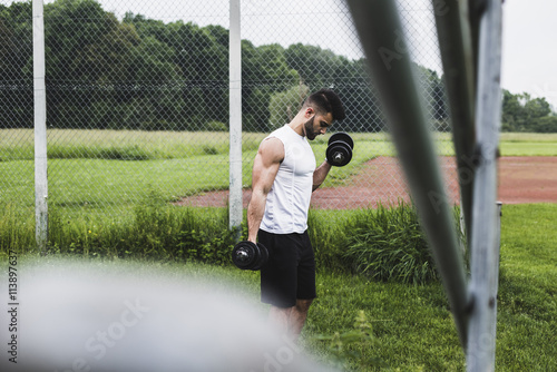 Athlete exercising with dumbbells on sports field photo