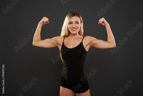  Fit blonde in sportswear showing muscular hands on black backgr