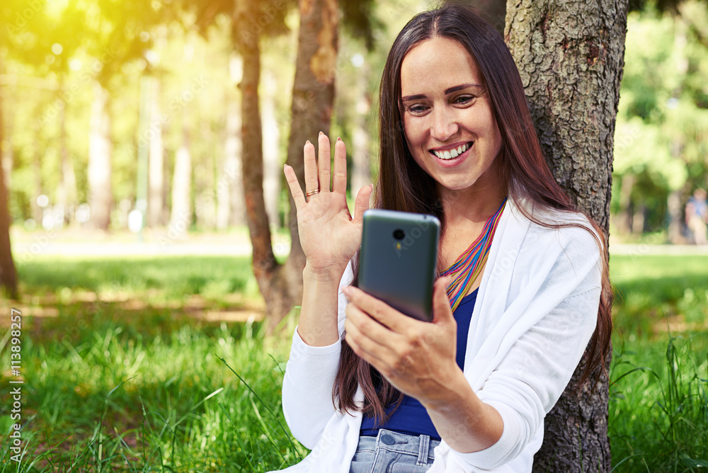 Smiling lady resting under tree and conducting a video call Smiling lady resting under tree and conducting a video call