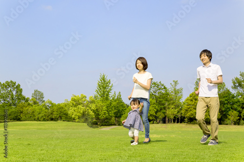 青空の下、芝生の公園で幼い女の子とt走る若い家族