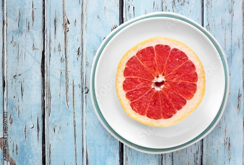 Fresh pink grapefruit half on plate with rustic blue wood background