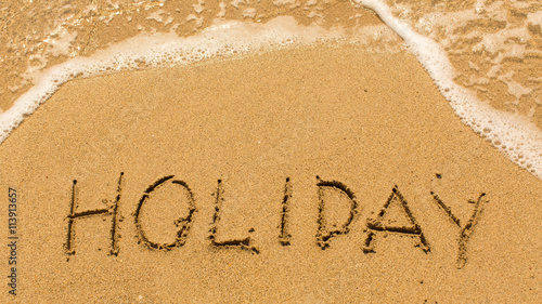 Holiday - inscription on sand beach with the soft wave.