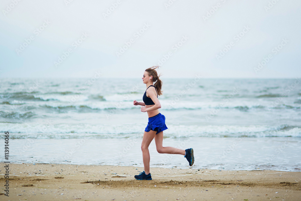 Young fitness running woman jogging on beach