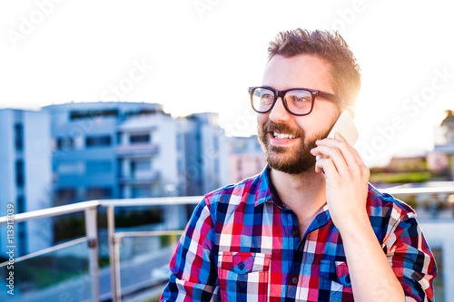 Businessman with smartphone making phone call, standing on balco photo