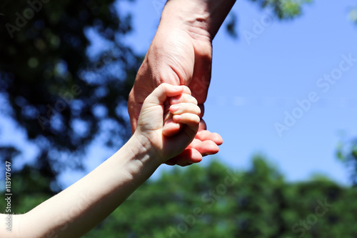 a father holds the hand of a small child on a green background © Saklakova