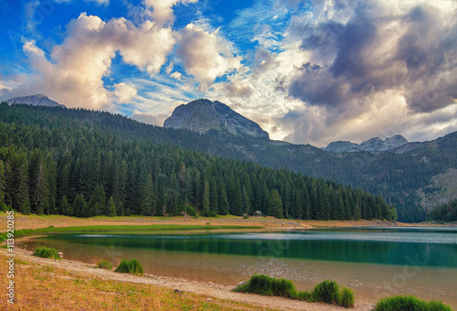 Black lake in Durmitor national park in Montenegro, Europe. Mountain, forest and beach on blue cloudy sky a sunny day at sunset. Beautiful landscape