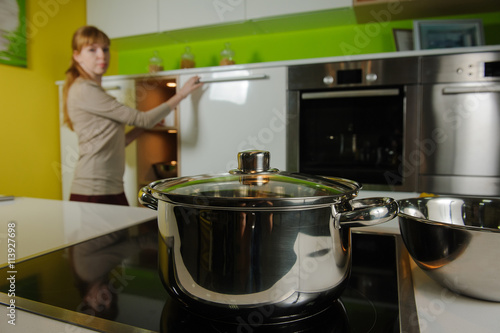 Pan on electric stove in the kitchen. Redhead woman cooking soup in home kitchen.