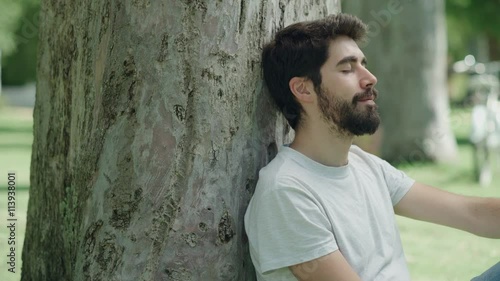 Young man resting pacefully sitting in the park. Close up. Dolly shot photo