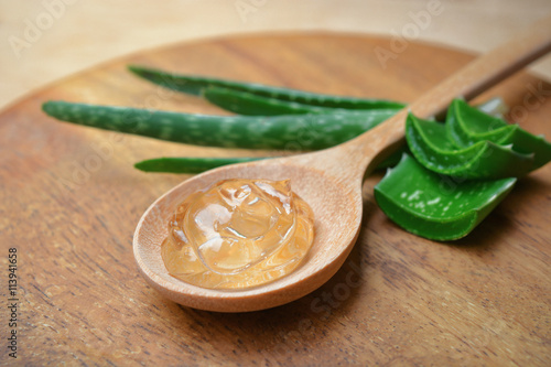Aloe vera gel on wooden spoon with aloe vera leaves on wooden board.