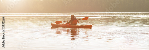 Man paddles canoe in river at sunrise