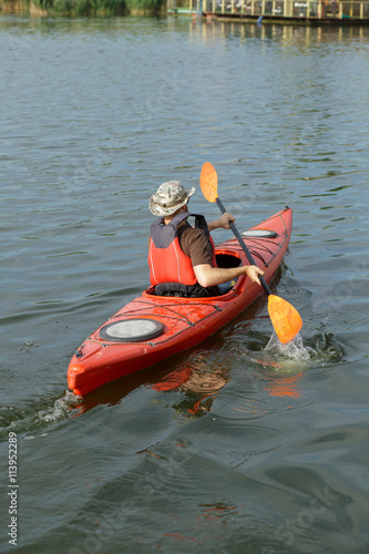 Man boating in red canoe in river at summer day, back view