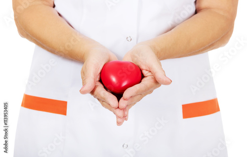 Elderly female doctor or nurse holding red toy heart