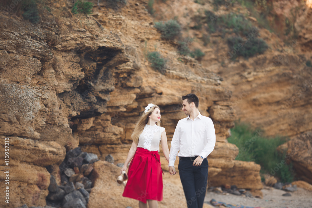 Fototapeta premium Romantic loving couple walking on the beach with rocks and stones