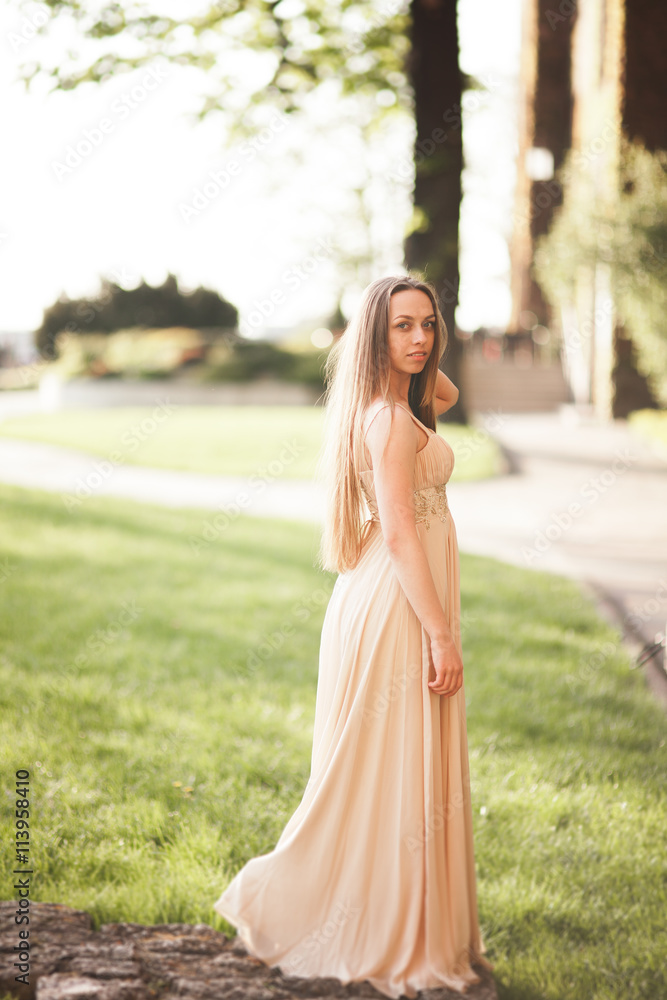 Attractive young woman with long dress enjoying her time outside in park sunset background Attractive young woman with long dress enjoying her time outside in park sunset background