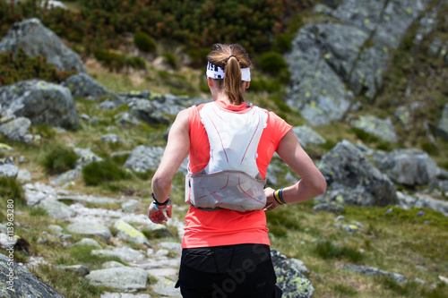 ultra trail runner woman with backpack training running in high mountains terrain