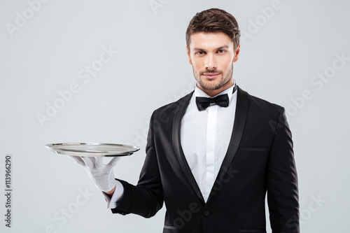 Obraz na płótnie Portrait of young butler in tuxedo holding empty tray